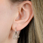 Nahaufnahme eines Ohrs, das den Liebeskind Berlin Ohrring von Liebeskind Berlin, einen silbernen Ohrring in Form einer Kaffeetasse, trägt, wobei hellbraunes Haar sichtbar ist.