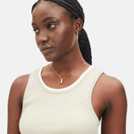 Frau mit geflochtenem Haar trägt ein beigefarbenes Tanktop, ein weißes Unterhemd, kleine Ohrringe und die LIEBESKIND BERLIN Halskette - The Love Lock von Liebeskind Berlin.