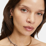 Frau trägt eine Kette aus gemischtem Metall und den Ohrring Creole - The Basic Bicolor von Liebeskind Berlin und schaut in die Kamera.