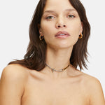 Frau mit braunen Haaren trägt die LIEBESKIND BERLIN Creole - The Basic Bicolor Ohrringe von Liebeskind Berlin, gepaart mit mehrlagigen Halsketten und einem schwarzen trägerlosen Oberteil.