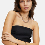 Eine Frau in einem schwarzen trägerlosen Top trägt die Liebeskind Berlin Halskette - The Secure Tag mit Edelstahlgliederkette und passendem Armband und posiert vor einem weißen Hintergrund.