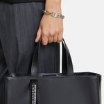 Eine Person in dunkler Hose trägt das LIEBESKIND BERLIN Armband - The Secure Tag von Liebeskind Berlin an einem Handgelenk.