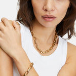 Frau in einem weißen Tank-Top trägt das LIEBESKIND BERLIN Armband - The Secure Tag von Liebeskind Berlin, gepaart mit einer goldenen Halskette. Ideal für Damen Schmuck Fans, die mühelose Eleganz schätzen.