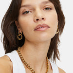 Frau trägt ein weißes Tanktop, goldene Ohrringe und die LIEBESKIND BERLIN Halskette - The Organic von Liebeskind Berlin und schaut in die Kamera.