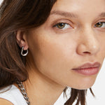 Frau mit heller Haut und braunen Haaren trägt The Organic Creole von Liebeskind Berlin und eine Kettenhalskette mit abnehmbarem Anhänger und schaut in die Kamera.