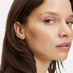 Eine Frau mit braunem Haar trägt einen kleinen LIEBESKIND BERLIN Creole - The Organic Creole Ohrring von Liebeskind Berlin und blickt vor einem hellen Hintergrund leicht zur Seite.