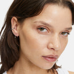 Eine Frau mit heller Haut und braunem Haar trägt zwei kleine silberne Ohrringe, gestylt mit dem LIEBESKIND BERLIN Ear Cuff - The Twisted von Liebeskind Berlin, und schaut in die Kamera.
