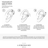 Schritt-für-Schritt-Anleitung zum richtigen Anlegen eines LIEBESKIND BERLIN Earcuffs. Drei schwarz-weiße Illustrationen zeigen, wie der Ear Cuff ohne Ohrloch vorsichtig an der oberen Ohrkante angesetzt, entlang der Ohrmuschel positioniert und wieder abgenommen wird.