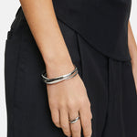 Eine Person trägt den LIEBESKIND BERLIN Ring - The Twisted Organic, Größe 56 von Liebeskind Berlin und ein passendes silbernes Armband, gestylt mit einer schwarzen Hose und einem schwarzen Top.