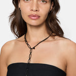 Eine Frau in einem schwarzen trägerlosen Top trägt die Liebeskind Berlin Halskette - Two Chain und schwarze Ohrstecker als stilvollen Schmuck vor einem weißen Hintergrund.