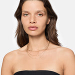 Eine Frau mit hellbraunem Haar trägt ein trägerloses schwarzes Oberteil und die LIEBESKIND BERLIN Halskette - Sparkling With Layers von Liebeskind Berlin, gestylt als elegantes Accessoire vor einem strahlend weißen Hintergrund.