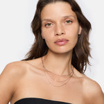 Frau mit gewelltem braunem Haar trägt ein schwarzes trägerloses Top und die LIEBESKIND BERLIN Halskette - Sparkling With Layers von Liebeskind Berlin und posiert selbstbewusst.