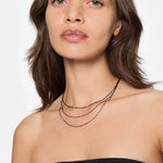 Eine Frau, die ein schwarzes trägerloses Top und die LIEBESKIND BERLIN Halskette - Sparkling With Layers von Liebeskind Berlin trägt, schaut selbstbewusst in die Kamera.