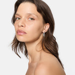 Frau mit gewelltem braunem Haar trägt LIEBESKIND BERLIN Creole - Sparkling Link Ohrringe von Liebeskind Berlin und blickt in die Kamera vor einem schlichten Hintergrund.