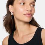 Frau mit schwarzem Tank-Top trägt die LIEBESKIND BERLIN Creole - Sparkling Link Ohrringe von Liebeskind Berlin mit schimmernden Zirkonia, die vor einem schlichten Hintergrund zur Seite blicken.
