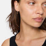 Frau mit hellbraunem Haar, trägt ein schwarzes Oberteil und LIEBESKIND BERLIN Creole - Sparkling Link Ohrringe von Liebeskind Berlin, schaut zur Seite.
