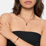 Frau in einem schwarzen trägerlosen Oberteil stylt die Liebeskind Berlin Halskette - Mini Link und das passende Armband - dieses trendige Set besteht aus kleinen rechteckigen schwarzen Anhängern für einen schicken, modernen Look.