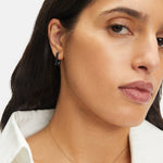 Frau mit langen dunklen Haaren trägt ein weißes Hemd, eine goldene Halskette und LIEBESKIND BERLIN Creole - Mini Link Ohrringe von Liebeskind Berlin, um ihrem Look einen Hauch von Statement-Schmuck zu verleihen.