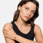 Eine Frau mit glattem braunem Haar in einem schwarzen ärmellosen Oberteil posiert mit einem gekreuzten Arm und trägt das LIEBESKIND BERLIN Armband - Urban Heart von Liebeskind Berlin.