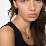 Frau mit langen braunen Haaren in einem schwarzen Tank-Top, trägt eine goldene Halskette und die Liebeskind Berlin Creole - Urban Heart Ohrringe für einen eleganten Touch.
