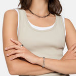 Frau in beigefarbenem Tank-Top verschränkt die Arme und trägt die Liebeskind Berlin Halskette - Urban Chic, zusammen mit einem Armband und einem Ring als Statement-Schmuck.