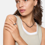 Frau in einem beigen Tank-Top trägt die LIEBESKIND BERLIN Halskette - Urban Chic von Liebeskind Berlin als Statement-Schmuck, gepaart mit Ohrringen und einem Ring, mit Blick zur Seite.