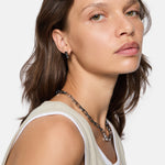 Frau mit braunen Haaren trägt ein ärmelloses beigefarbenes Oberteil, Kettenhalsband und LIEBESKIND BERLIN Creole - Urban Chic Ohrringe von Liebeskind Berlin, nach vorne schauend.