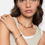 Eine Frau trägt roségoldenen Liebeskind Berlin-Schmuck, darunter die LIEBESKIND BERLIN Halskette - Urban Chic, Armband, Ohrringe und Ring, kombiniert mit einem neutralen Oberteil und natürlichem Make-up.