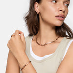 Frau im beigen Tanktop trägt den Liebeskind Berlin Urban Chic Ring in Größe 58, gepaart mit passendem Goldschmuck, während sie zur Seite schaut.