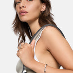 Frau mit gewelltem braunem Haar und Tanktop trägt LIEBESKIND BERLIN Creole - Urban Chic Ohrringe und hält einen Taschenriemen über der Schulter - ein elegantes Accessoire von Liebeskind Berlin.