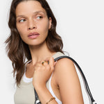 Frau mit gewellten braunen Haaren, trägt ein Tanktop und Goldschmuck mit groben Gliedern, darunter das LIEBESKIND BERLIN Armband - Urban Chic von Liebeskind Berlin, hält einen Taschenriemen und schaut zur Seite.