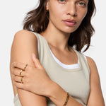 Frau mit beigem Tank-Top und goldenen Ringen posiert mit verschränkten Armen und trägt das Liebeskind Berlin Armband - Urban Chic.