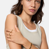 Frau in einem beigen Tank-Top trägt den Liebeskind Berlin Ring - Urban Chic in 54, ein goldenes Armband und kleine goldene Ohrringe.