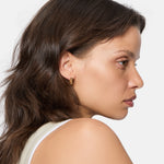 Frau mit braunen Haaren im Profil trägt ein ärmelloses Oberteil und stilvolle Liebeskind Berlin Creole - Urban Chic Ohrringe, ein Must-Have-Accessoire, vor einem weißen Hintergrund.