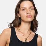 Frau mit gewelltem braunem Haar trägt ein schwarzes Tanktop und eine goldene Liebeskind Berlin Halskette - The T-Bar Plate.