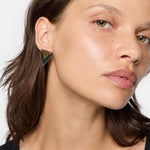 Eine Frau mit grünen Augen trägt LIEBESKIND BERLIN Ohrhänger - The Geometric von Liebeskind Berlin, die einen urbanen Stil mit einem Hauch von 70er-Jahre-Look zeigt.