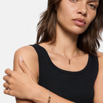 Frau im schwarzen Tank-Top trägt eine goldene LIEBESKIND BERLIN Halskette - Mini Link und ein dazu passendes Armband und schaut in die Kamera.