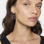 Frau mit hellbraunem Haar und schwarzem Oberteil trägt LIEBESKIND BERLIN Creole - Big Link Ohrringe von Liebeskind Berlin und schaut leicht zur Seite.