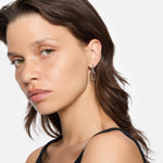 Frau mit braunen Haaren trägt ein schwarzes Oberteil und LIEBESKIND BERLIN Creole - The Mini Link Ohrringe von Liebeskind Berlin in zeitlosem Design und schaut in die Kamera.