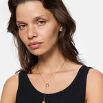 Frau mit gewelltem braunem Haar trägt ein schwarzes Tank-Top und die LIEBESKIND BERLIN Halskette - The Organic Twist, posiert vor einem weißen Hintergrund. Ein stilvolles Beispiel für die Schichtung von Gold- und Edelstahl-Halsketten von Liebeskind Berlin.