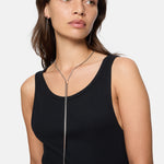 Frau in schwarzem Tank-Top trägt die Liebeskind Berlin Halskette - The Everyday Combination mit einem langen silbernen vertikalen Balkenanhänger.