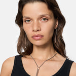 Eine Frau mit hellbraunem Haar trägt ein schwarzes Tank-Top und Liebeskind Berlin-Schmuck, darunter The Everyday Combination Ohrhänger, und schaut in die Kamera.