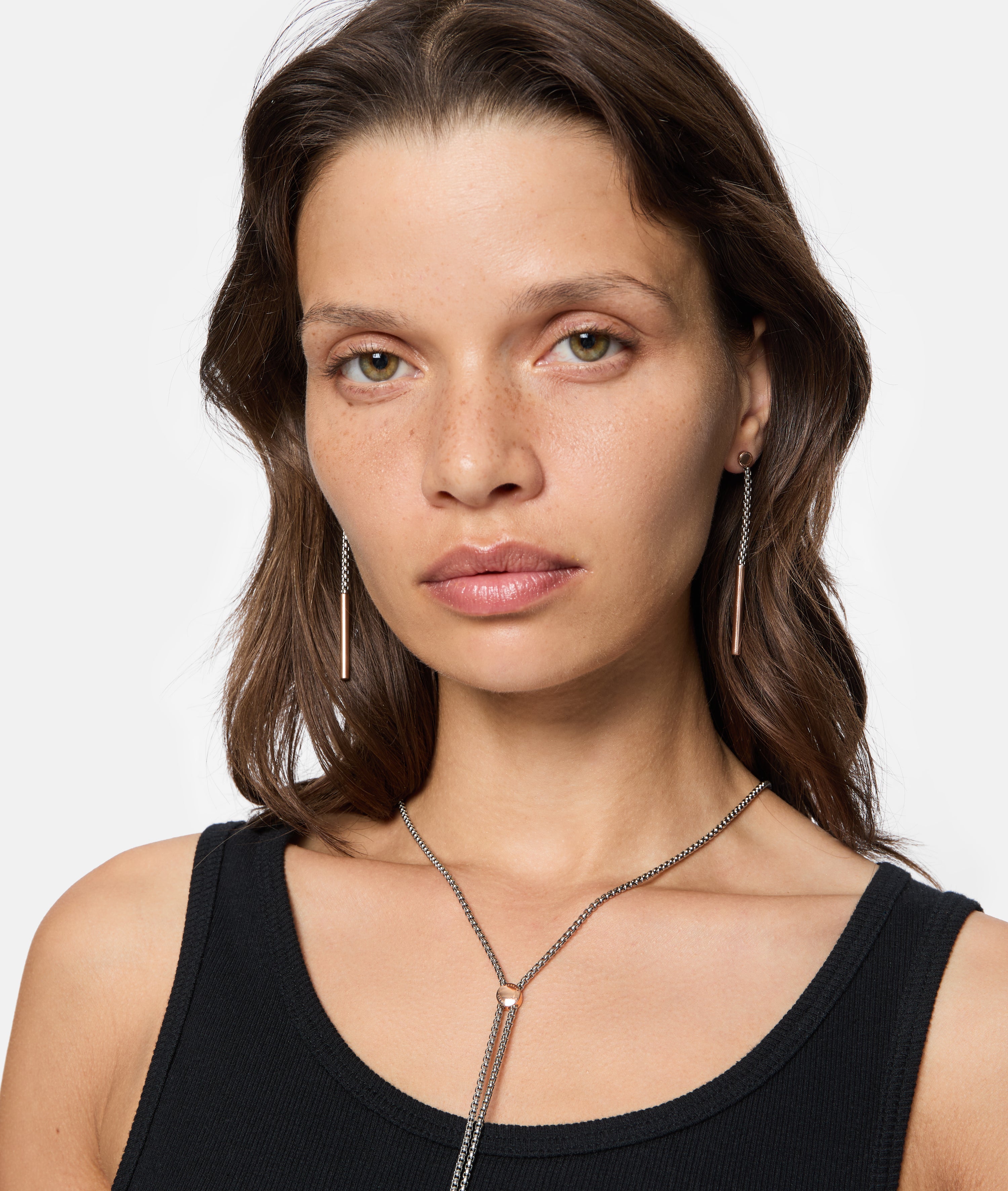 Eine Frau mit hellbraunem Haar trägt ein schwarzes Tank-Top und Liebeskind Berlin-Schmuck, darunter The Everyday Combination Ohrhänger, und schaut in die Kamera.