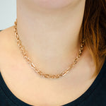 Eine Frau, die die Liebeskind Berlin Halskette - The Double Tag und ein dunkles Oberteil trägt, wobei ihr Haar über eine Schulter fällt.