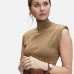 Frau in ärmellosem hellbraunem Rollkragenpullover und brauner Hose, die filigran geprägten Münzschmuck und das Liebeskind Berlin Armband - Vintage Coins trägt und zur Seite schaut.