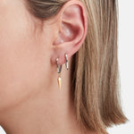 Nahaufnahme des Ohrs einer Person mit zwei silbernen Liebeskind Berlin Creole - The Pendulum-Ohrringen, einer davon mit einem goldenen Anhänger, und kurzem blondem Haar.