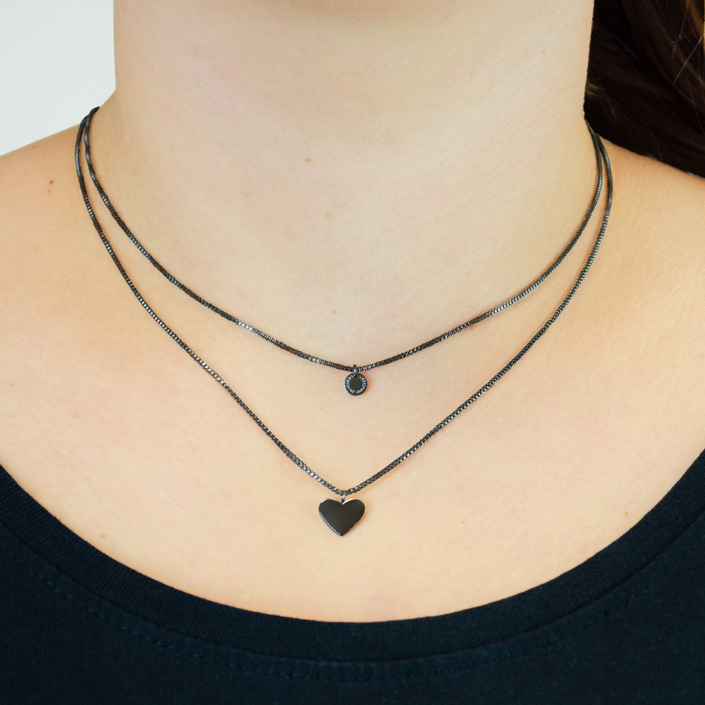 Eine Person trägt zwei silberne Halsketten - eine mit einem kleinen schwarzen Stein und eine mit einem schwarzen Herz - aus dem Liebeskind Berlin LIEBESKIND BERLIN Set - Everyday Layering Black, gepaart mit schwarzen Ohrsteckern für einen modernen Lagenlook.