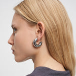 Eine Frau mit glattem blondem Haar, von der Seite gesehen in einem grauen Oberteil, trägt LIEBESKIND BERLIN Creole - Steel Ball Ohrringe von Liebeskind Berlin.