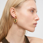 Frau mit glattem blondem Haar trägt Liebeskind Berlin Creole - Steel Ball Ohrringe, gestylt mit einem braunen Neckholder-Top, von rechts.