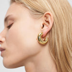 Blonde Frau trägt klobige LIEBESKIND BERLIN Creole - Steel Ball Ohrringe und mehrere kleine Silberohrringe, gestylt von Liebeskind Berlin.